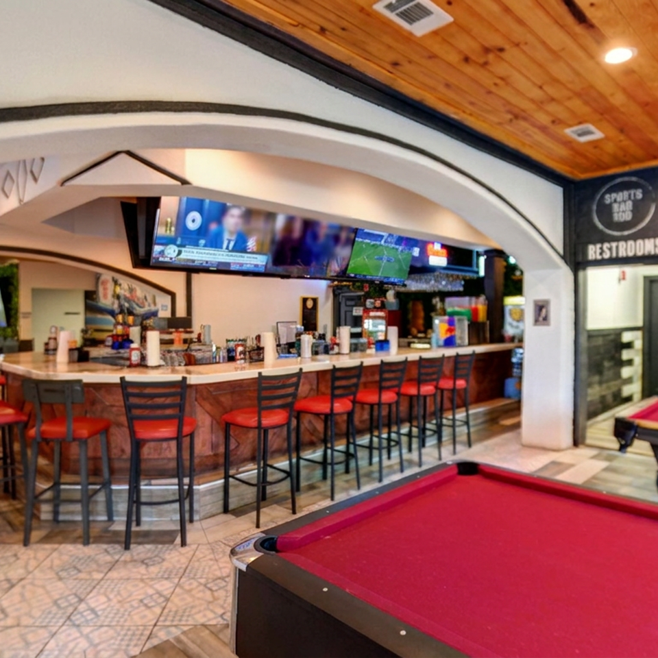 Sports bar with a long counter, red stools, televisions, and two red-felt pool tables beneath a wood-paneled ceiling.