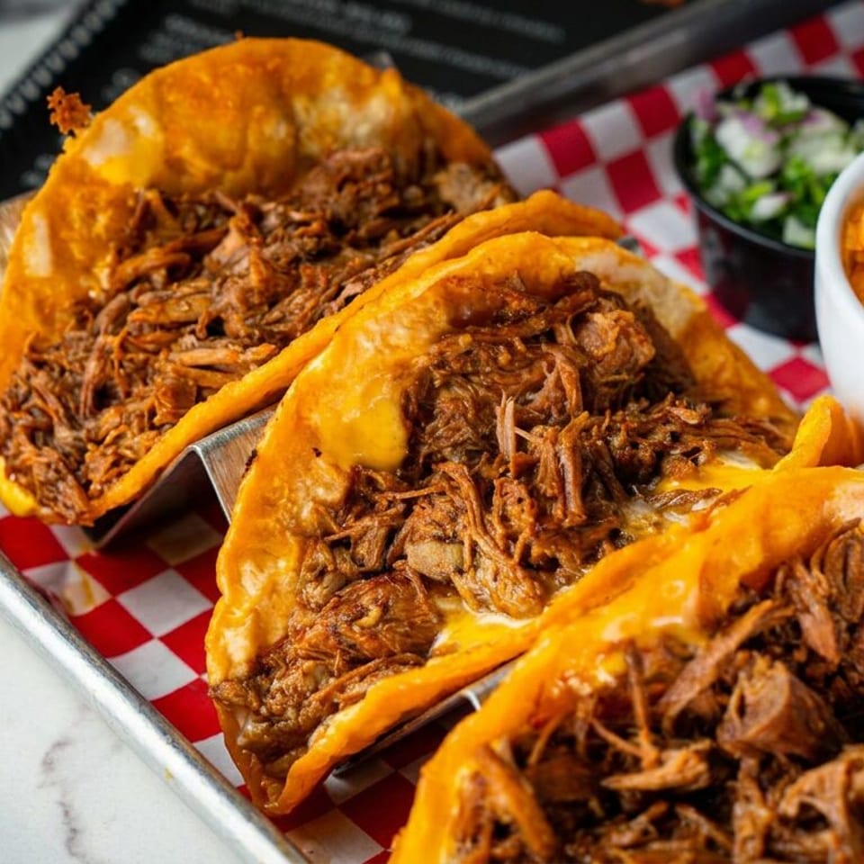 Three crispy shredded-beef tacos served with orange rice and salsa on a red-and-white checkered tray liner.