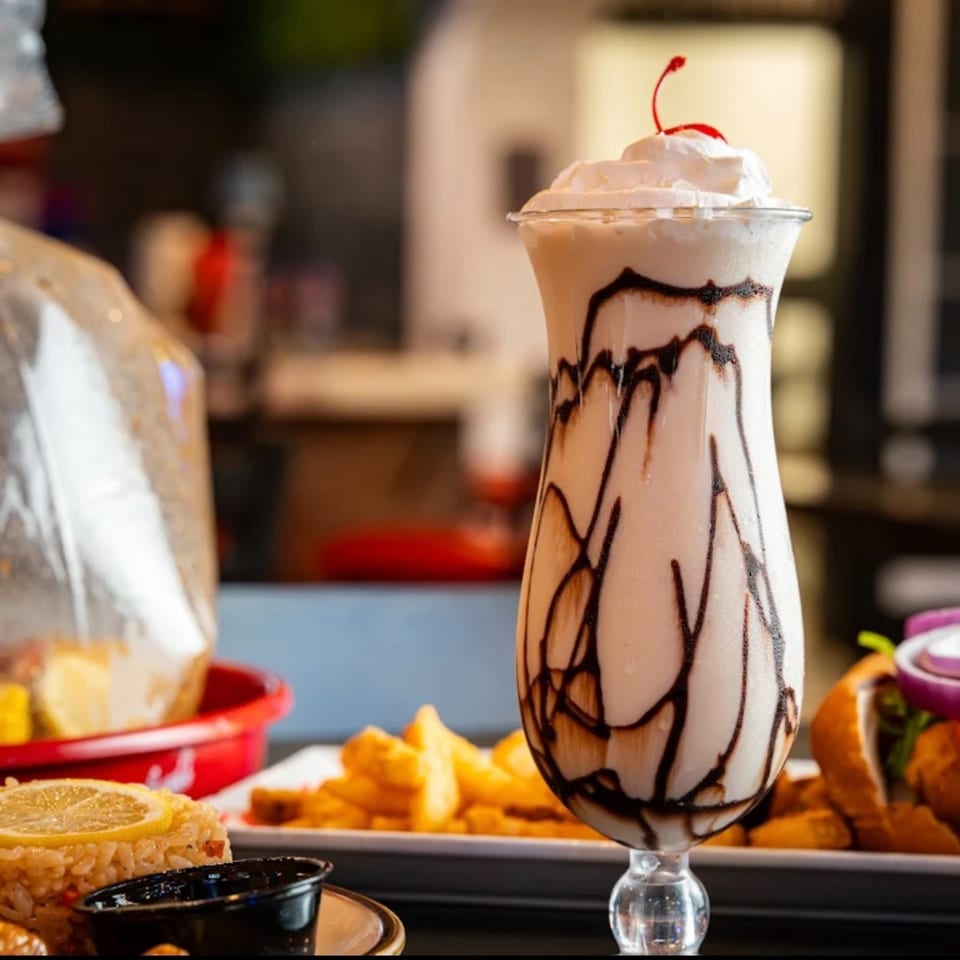 Chocolate milkshake with whipped cream and a cherry, alongside rice, fries, and a burger.